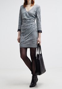 Šedé texturované šaty s překládaným designem, V-výstřihem a třičtvrtečními rukávy. Doplněné černými punčochami a černou kabelkou.