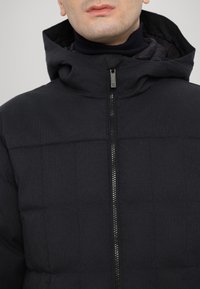 Black padded jacket with a hood, featuring a quilted design and a front zipper. Made of textured fabric, the collar is high and snug.
