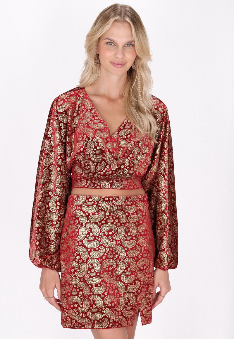 Ein rotes und goldenes Paisleymuster-Outfit mit einem bauchfreien Oberteil, das lange Ärmel hat, und einem passenden Rock mit einem seitlichen Schlitz.