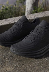 Paire de chaussures de sport noires avec un design à lacets reposant sur une surface en béton rugueuse à l'extérieur.