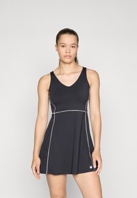 Vestido atlético preto com decote em V, apresentando um piping branco ao longo das costuras. Textura suave, corpete ajustado e saia evasê. Logotipo simples na bainha.