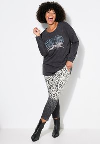 Maglietta nera a maniche lunghe con grafica "Stay Wild", abbinata a leggings con stampa leopardata che sfuma dal chiaro allo scuro. Stivali neri alla caviglia.