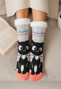 Calze lavorate a maglia con un design di un gatto nero, sfondo grigio, accenti corallo e un polsino bianco in soffice tessuto. Motivi ondulati in blu e rosso.