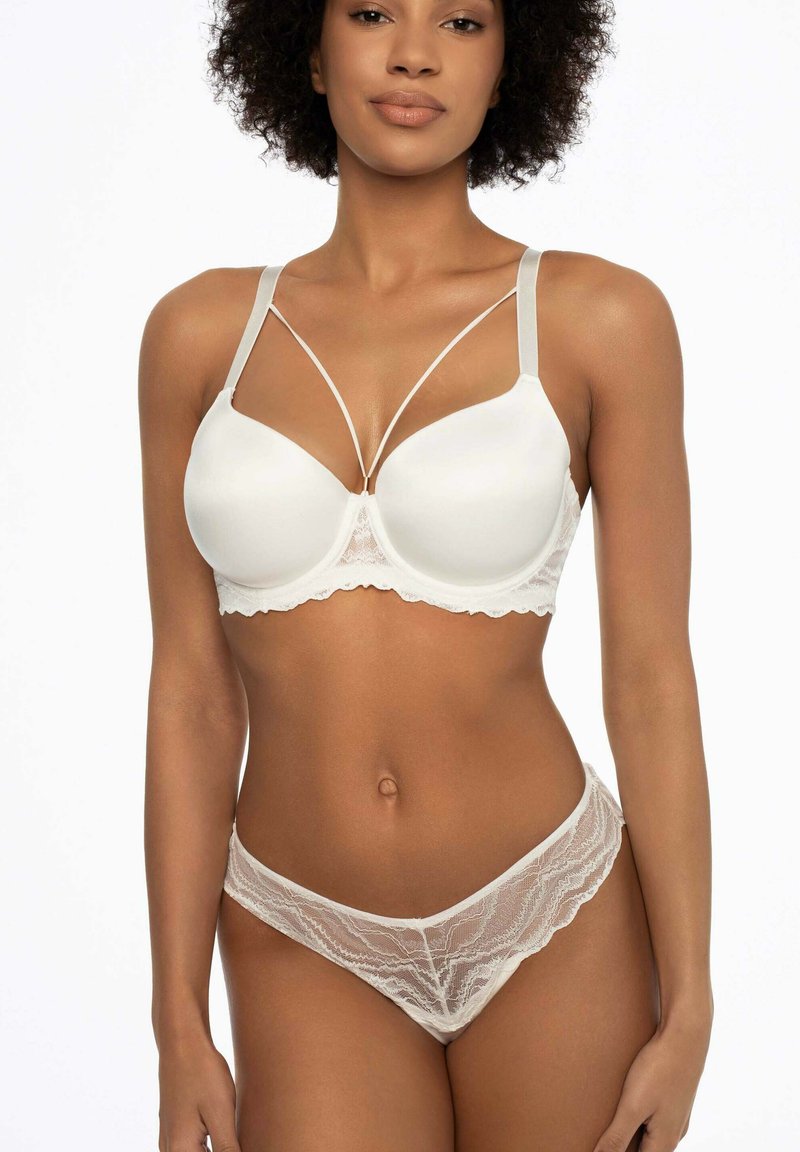 Biały koronkowy zestaw bielizny składający się z gładkiego, wyściełanego biustonosza z krzyżującymi się ramiączkami oraz dopasowanego, przezroczystego koronkowego Stringa z falbaniastymi brzegami.