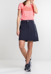 Camisa corta de mangas, en coral, con escote en V y un diseño gráfico; falda corta navy con bolsillos frontales; combinada con zapatillas deportivas negras.