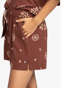 Shorts floraux marron avec une coupe décontractée, une taille élastique, des poches latérales et de subtils accents de boutons décoratifs. Matière légère en coton.