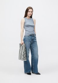 Gray sleeveless top, wide-leg blue jeans, holding a textured gray snake-patterned bag. Simple design with flat black shoes.