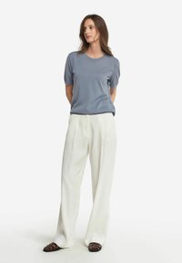 Ljuss blå t-shirt med kort ärm, kombinerad med höga vita byxor. Outfiten har en avslappnad passform och en mjuk textur. Bruna remsandaler.