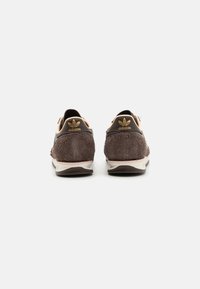 Baskets en suede marron avec des accents en cuir rose. Caractéristiques d'une forme arrondie, d'un design texturé et d'une marque dorée sur le talon. Semelle en caoutchouc.