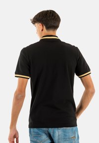 Polo nero a maniche corte, con accenti a righe dorate e nere nel colletto e nei bordi delle maniche. Materiale in cotone.