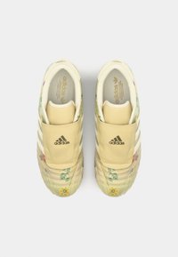 Žluté tenisky Adidas s květinovými vzory, texturovaným svrškem, elastickým designem a bílými pruhy. Mají polstrovaný límec a stélku.