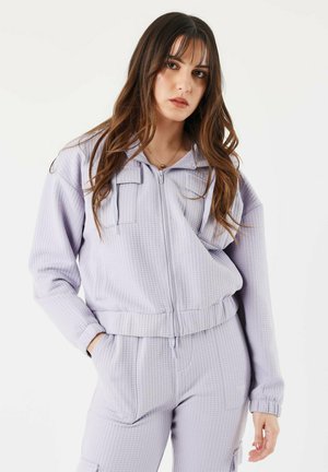 Lichtpaarse, gestructureerde trainingsoutfit met een ritsjack met twee borstzakken en elastische manchetten, gecombineerd met bijpassende broek.