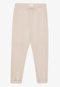 Beige taperte joggebukser med elastisk midje, snor, sidelommer og elastiske mansjetter, vist flatt på en hvit bakgrunn.