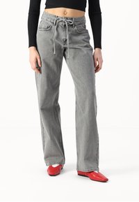 Jeans de tiro alto grises con cintura ajustable, bolsillos frontales y un corte relajado, combinados con zapatos rojos de punta cuadrada.