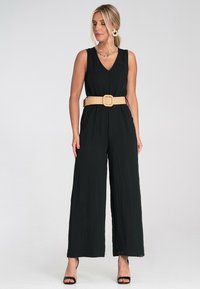 Czarny, bezrękawnikowy kombinezon z dekoltem w kształcie litery V, o teksturowanej tkaninie, szerokich nogawkach oraz beżowym, plecionym pasku z kwadratową klamrą.