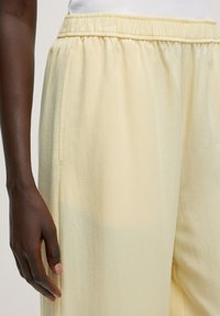 Lichtgele, ontspannen pasvorm broek met een elastische tailleband, zijzakken en zachte, gemeleerde stof. Eenvoudig ontwerp, gladde afwerking.