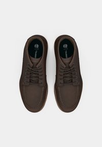 Brown leather shoes with stitched detailing, featuring round laces, a textured sole, and a black insole with a logo.
