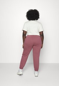 Valkoinen lyhythihainen t-paita yhdistettynä tummanpunaisiin collegehousuihin, joissa on elastiset hihnat, käytetään valkoisten lenkkarien kanssa, näkymä takaa.