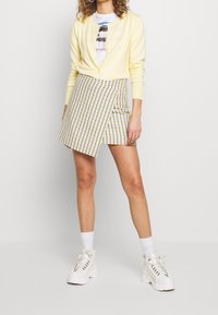 Żółty kardigan, biały t-shirt z grafiką, asymetryczna spódnica w kratkę w żółtym i niebieskim kolorze, zestawiona z masywnymi białymi trampkami i skarpetkami do kostek.