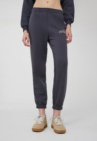 Ciemnoszare dresy z elastycznymi mankietami, z haftowanym logo "PHOENIX" na lewej udzie. Wykonane z miękkiego materiału, idealne do codziennego noszenia.