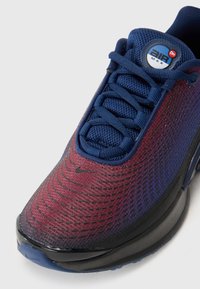 Plave i burgundske atletske tenisice s mrežastim gornjim dijelom, teksturiranom površinom, crnim potplatom i crnim Nike logom na prstu. Šnalanjem i podstavljenim ovratnikom.