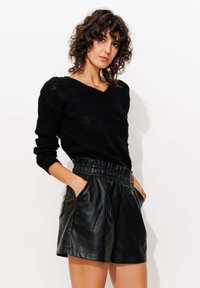 Pull en tricot noir à col en V et motif texturé, associé à un short en cuir noir taille haute avec poches latérales et ceinture élastique.