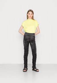 T-shirt amarelo crop combinado com calças pretas com pregas. As calças apresentam pregas verticais e uma cintura elástica, finalizadas com sandálias pretas.