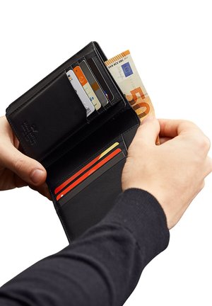 Mani che tengono un portafoglio in pelle nera con più carte e una banconota da 50 euro che viene inserita all'interno.