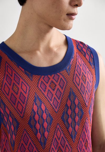 Maglione senza maniche lavorato a maglia con un motivo esagonale in rosso, blu e viola. Collo a girocollo con orlo blu a coste. Tessuto texturizzato.
