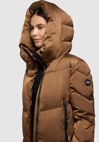 Rjava prešita puhovka z velikim kapuco, žepom z zadrgo in našitkom z logotipom. Material je gladek in rahlo sijoč.