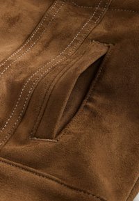 Braunes Wildledergewebe mit weicher Textur. Verfügt über eine genähte Tasche und weiße Nähte entlang der Nähte für zusätzliche Details.