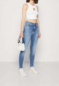 Ljusblå smala jeans i denim, kombinerade med en vit kortärmad tanktop med ett gult smiley-ansikte, och vita sneakers.