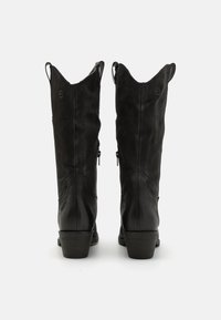Bottes de cowboy en cuir noir avec une finition en daim doux, bouts pointus, bords courbés, languettes de tirage et un petit talon épais.