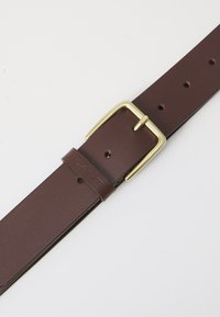 Cinturón de cuero marrón con una textura suave, que presenta una hebilla de metal color dorado y varios agujeros de ajuste. Marcado con "GANT."