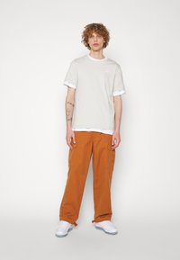 Svetlo šedé tričko s bielym lemovaním, spárované s oranžovými cargo nohavicami. Biely tenisky dopĺňajú outfit, pričom ukazujú neformálny, mestský štýl.