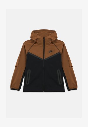 Corta-vento Nike com um design em bloco de cores castanho e preto, tecido leve, capuz e bolsos laterais com fecho de correr.