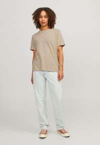 Beige katoenen T-shirt met een ronde hals en korte mouwen, gecombineerd met lichtblauwe recht gesneden jeans en bruine lage sneakers.