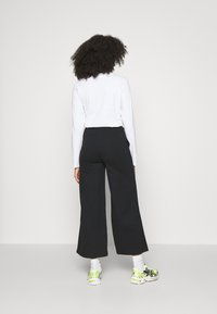 Svart vida byxor, hög midja, ihop med en långärmad vit topp och sneakers med neondetaljer, sedd bakifrån.