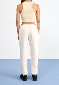 Beige ribbineulecrop-top, jossa on pyöreä pääntie, yhdistetty valkoisiin verkkareihin, joissa on joustava vyötärönauha ja sivutaskut, pukeutuneena mustiin lenkkareihin.