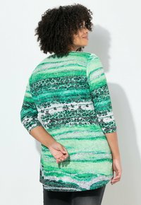 Zielona tunika w paski z akcentami w zwierzęcy wzór. Posiada rękawy do połowy przedramienia, luźny krój oraz zaokrąglony dół. Wykonana z miękkiej, teksturowanej tkaniny.