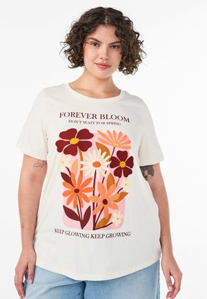 Kvinde iført creme t-shirt med farverig blomst illustration og tekst "Forever Bloom, Vent ikke på foråret, Bliv ved med at skinne, Bliv ved med at vokse."