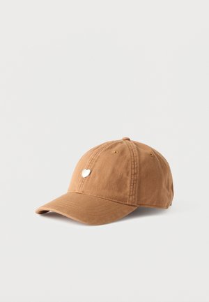 Brązowa bawełniana czapka z daszkiem z małą srebrną przypinką w kształcie serca na przedniej części, na jednolitym białym tle.