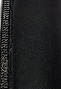 Gros plan d'un matériau en cuir noir avec une couture serrée à côté d'une fermeture éclair métallique noire sur le côté gauche.