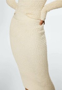 Béžové pletené šaty s texturou a vypasovaným střihem, které mají jemný pas a žebrované akcenty po délce sukně.