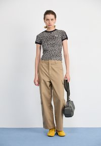 Top s leopardím vzorem, dobře padnoucí, s černými detaily, béžové cargo kalhoty a žluté boty. Šedá kabelka s ramenním popruhem.