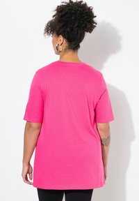 Camiseta de manga corta rosa con un corte relajado, hecha de una tela suave. Presenta un escote redondo y se extiende ligeramente por debajo de las caderas.