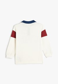 Camisa polo blanca de manga larga con cuello azul oscuro y detalles de malla roja en las mangas; tejido ligero y texturizado.