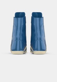 Blue glossy ankle boots with a textured cream sole, featuring a smooth design and raised heel for added stability.