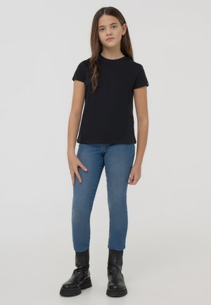 T-shirt nera a maniche corte in cotone, abbinata a jeans skinny blu e stivali neri alla caviglia. Design semplice con scollatura rotonda.