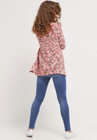 Blommönstrad långärmad topp i rosa, röd och blå nyanser, i kombination med blå tajta jeans. Mjuk, texturerad tyg med ett flödande design.